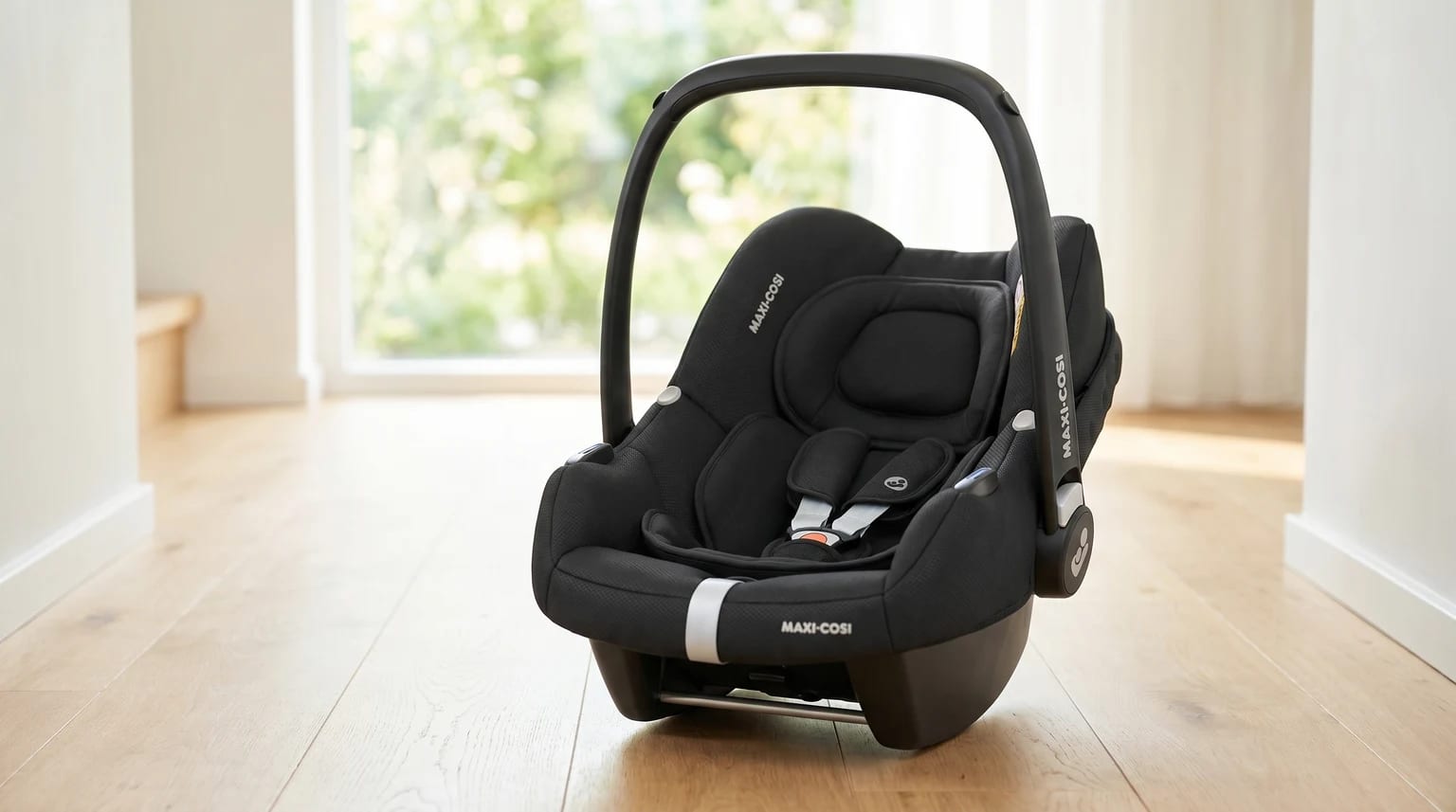 Cadeira auto Maxi-Cosi CabrioFix i-Size preta, pousada num chão de madeira clara numa casa moderna e bem iluminada.