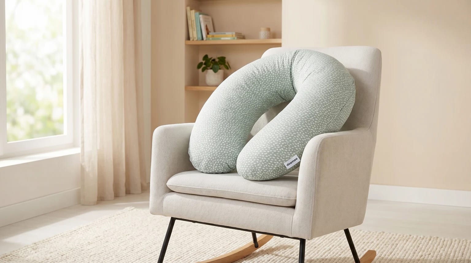 Almofada de amamentação e gravidez Doomoo Buddy, de cor verde-claro com padrão, pousada confortavelmente numa cadeira de baloiço num quarto de bebé luminoso e calmo.