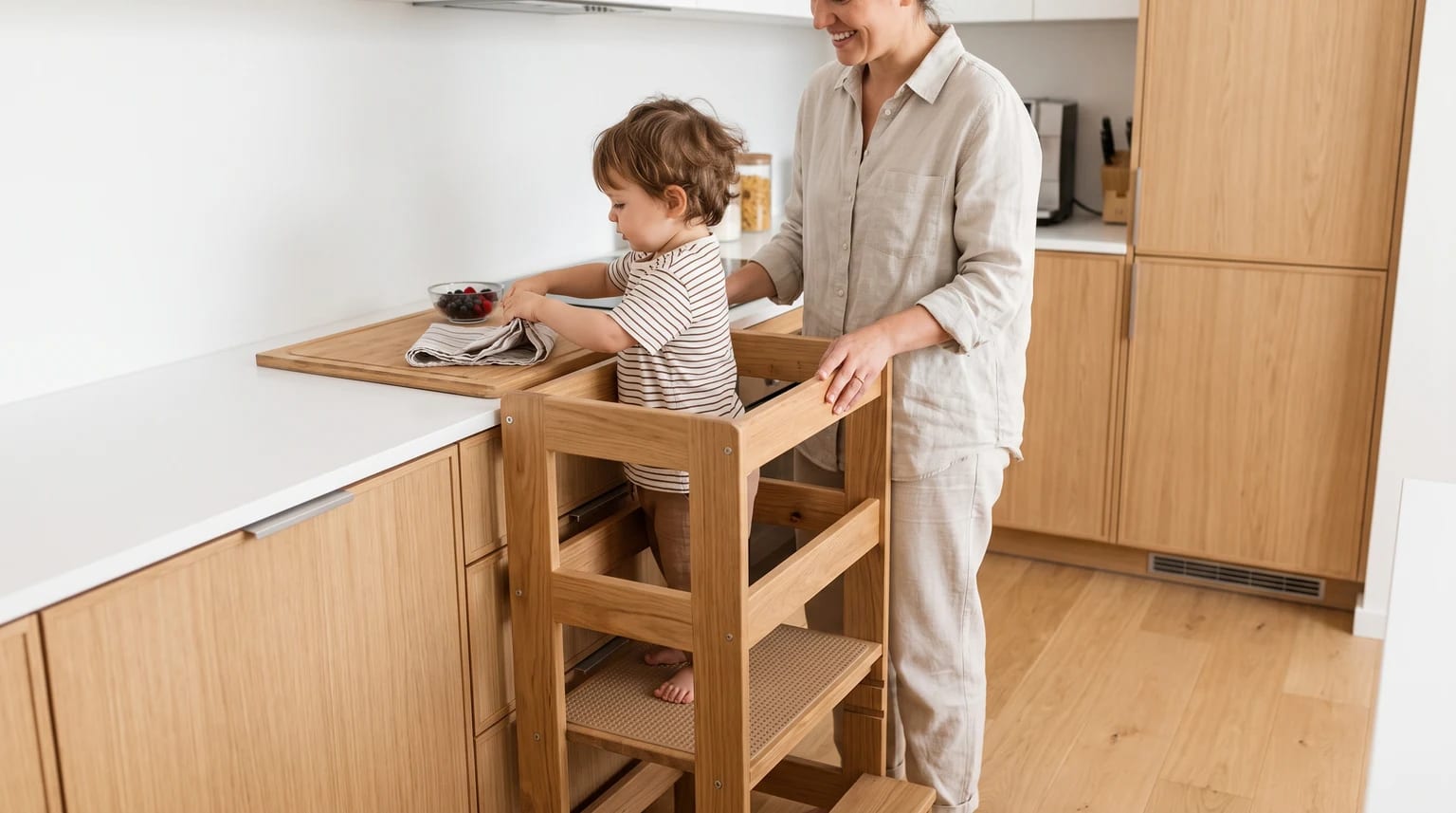 Criança numa torre de aprendizagem Montessori com adulto ao lado numa cozinha moderna