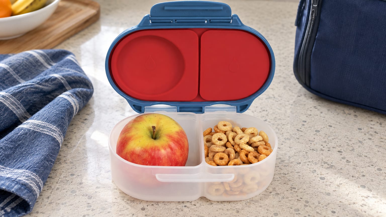 Caixa b.box Snackbox aberta com fruta e cereais numa bancada de cozinha.