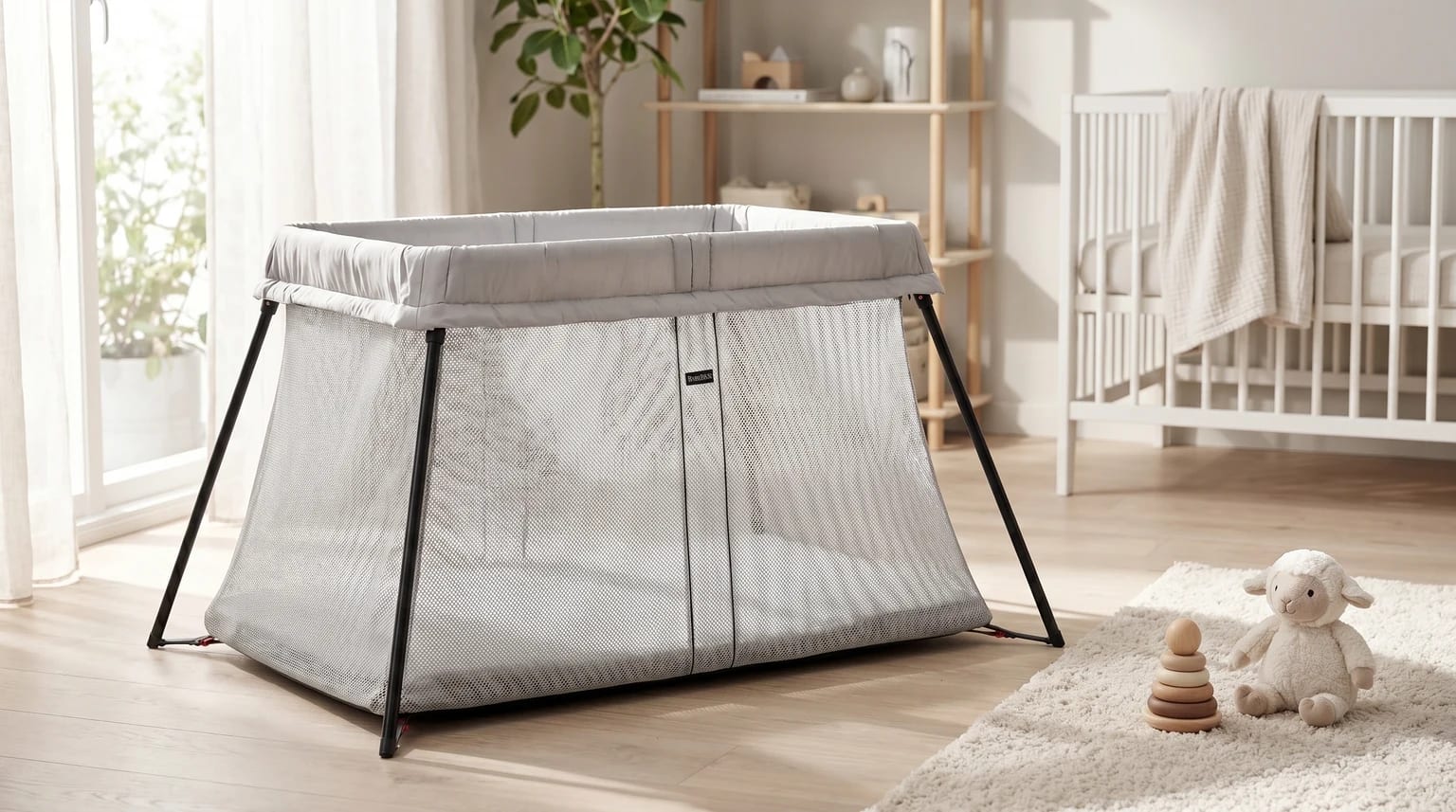 Berço de viagem BabyBjörn cinzento claro, montado num quarto de bebé moderno e luminoso, com tapete felpudo e brinquedos no chão.