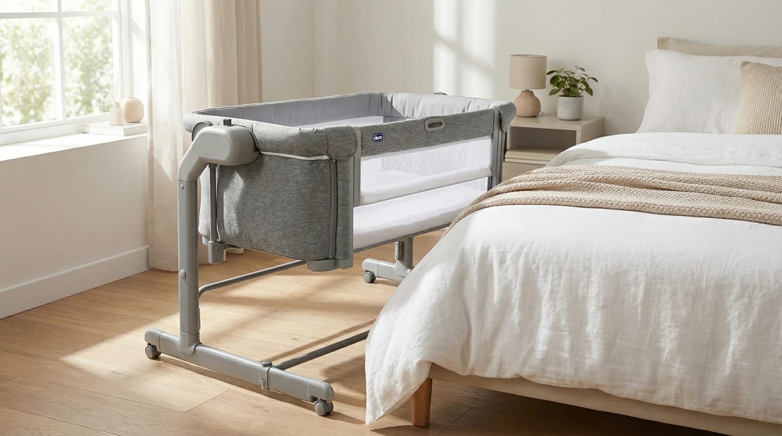 Berço co-sleeping Chicco Next2Me Magic EVO cinzento, posicionado ao lado de uma cama num quarto moderno e luminoso.