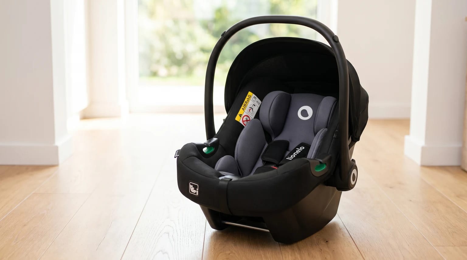 Cadeira auto para bebé Lionelo Astrid, em preto e cinzento, pousada num chão de madeira clara numa divisão moderna e luminosa.