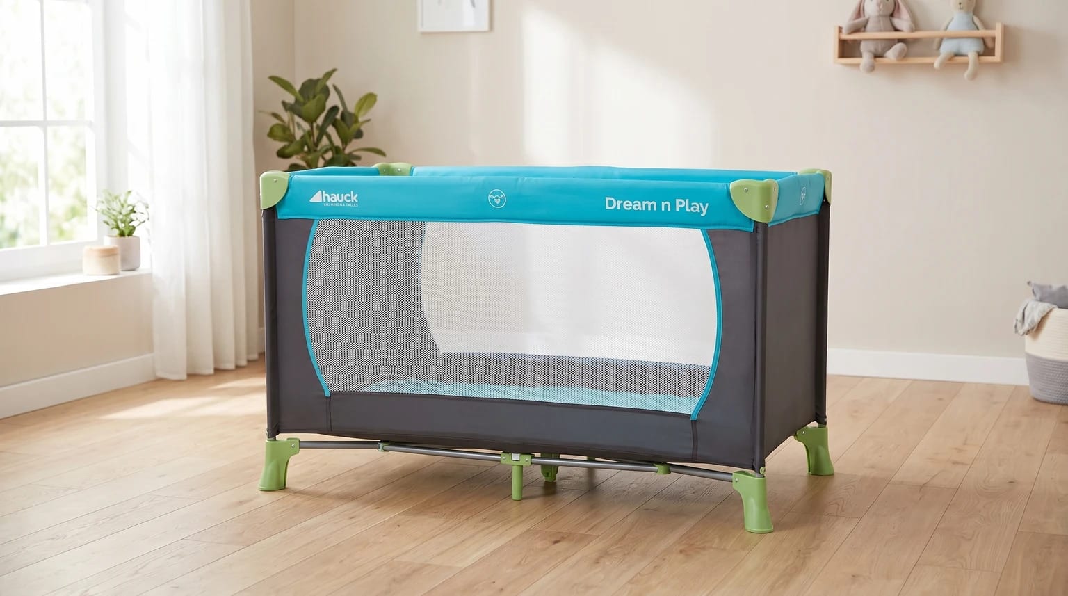 Cama de viagem Hauck Dream N Play azul e cinza, montada num quarto de bebé moderno e luminoso com chão de madeira clara.