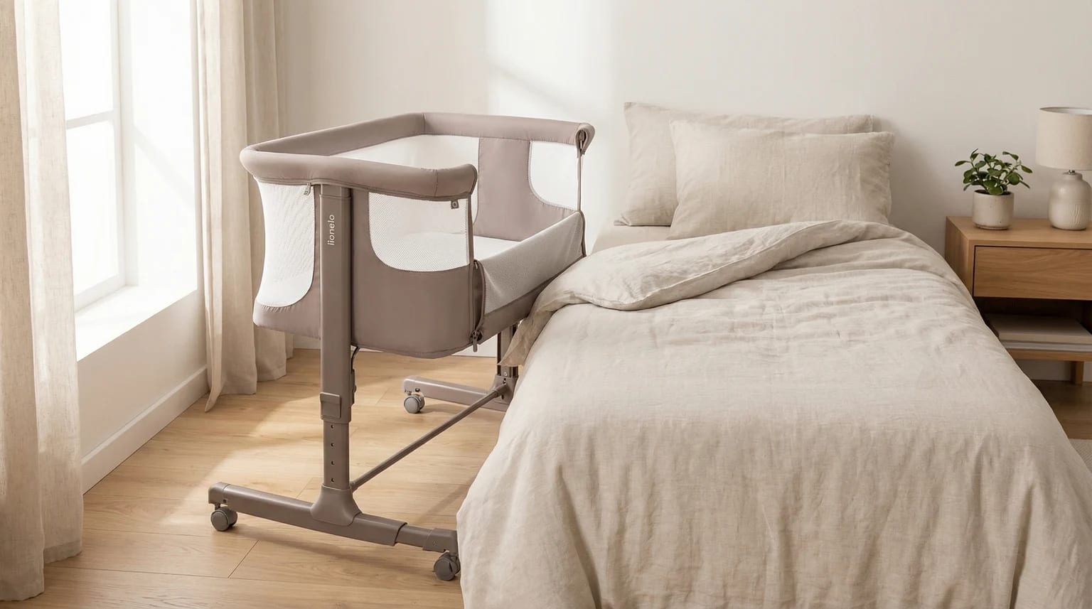Berço co-sleeper Lionelo Aurora em cinzento-toupeira, colocado ao lado de uma cama de adulto num quarto de dormir sereno e bem iluminado.